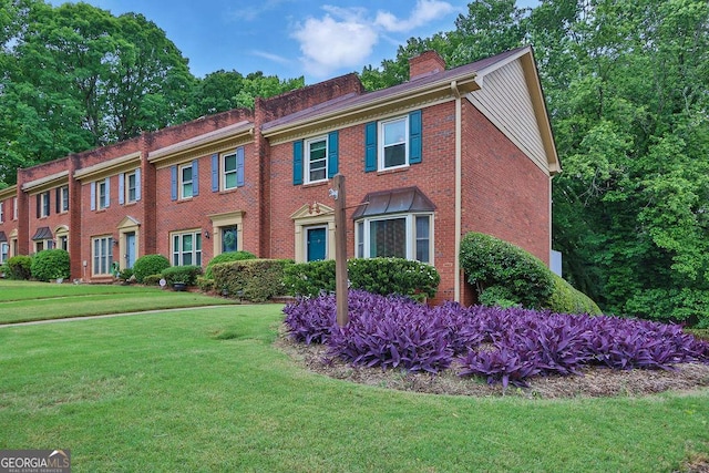 view of front of home featuring a chimney, brick siding, and a front lawn