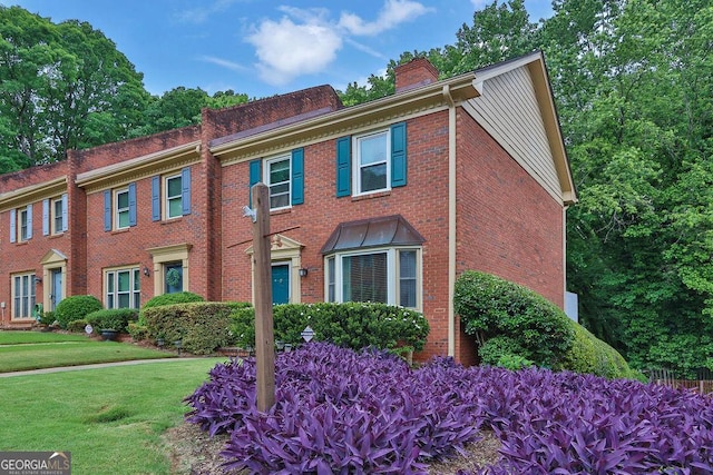 view of front of home featuring a chimney, brick siding, and a front lawn