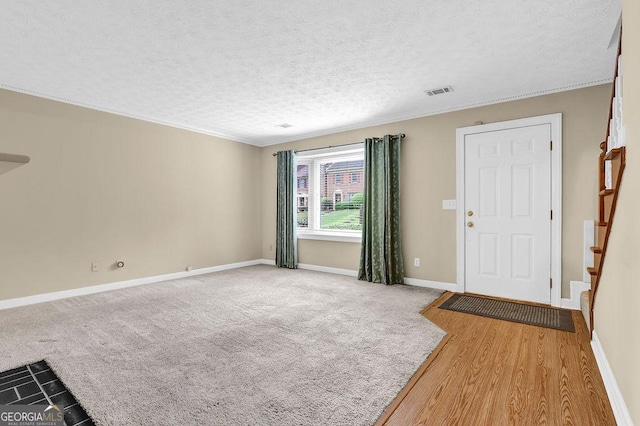 foyer entrance with baseboards, a textured ceiling, ornamental molding, stairway, and light wood-type flooring
