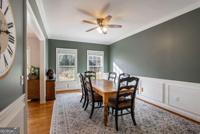 dining area featuring crown molding, ceiling fan, wood finished floors, and a wainscoted wall