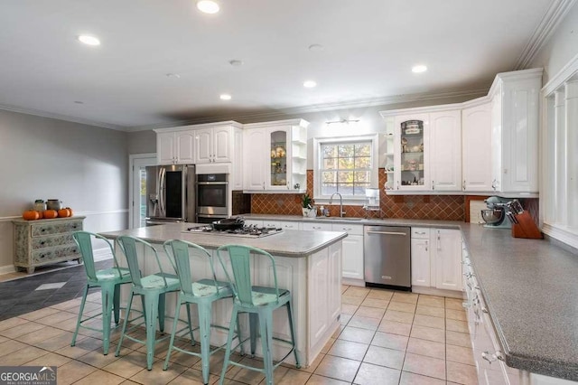 kitchen with a sink, a kitchen breakfast bar, stainless steel appliances, white cabinetry, and decorative backsplash