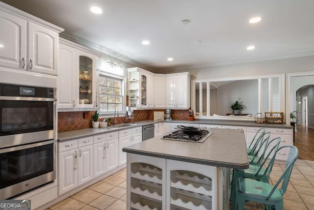 kitchen with a sink, a breakfast bar area, stainless steel appliances, light tile patterned floors, and glass insert cabinets