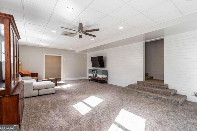 carpeted living room featuring ceiling fan, stairway, baseboards, a drop ceiling, and recessed lighting