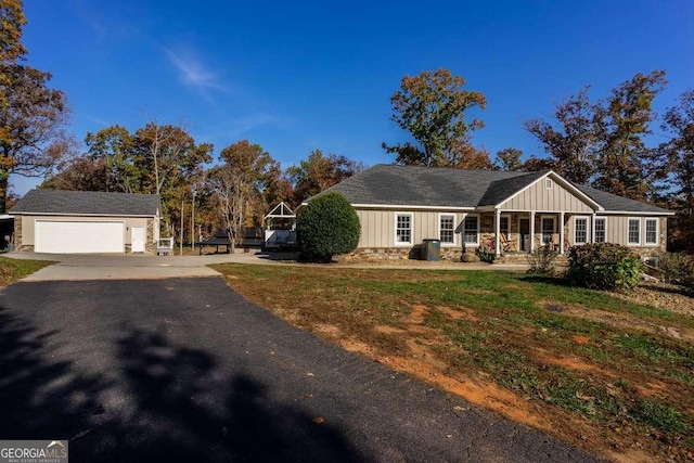view of front facade with a garage, driveway, stone siding, board and batten siding, and an outbuilding