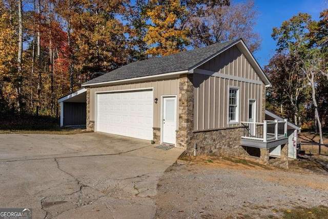 view of side of home featuring a shingled roof, stone siding, a detached garage, board and batten siding, and driveway