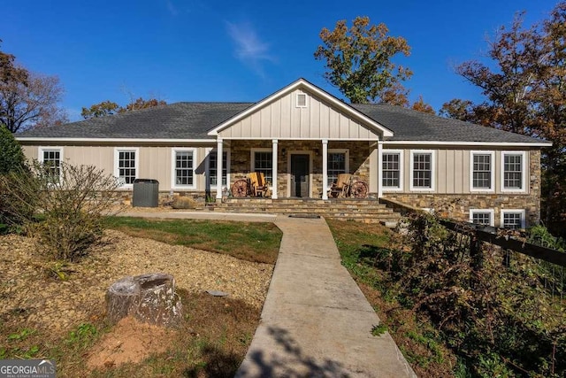 view of front of house with covered porch, board and batten siding, roof with shingles, central AC unit, and stone siding
