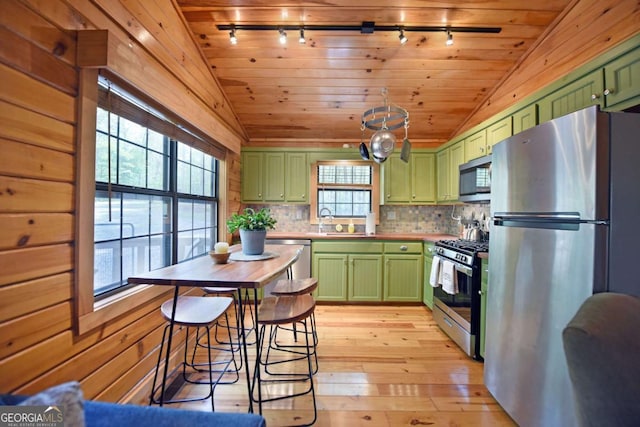kitchen with appliances with stainless steel finishes, rail lighting, light wood-style flooring, vaulted ceiling, and green cabinets