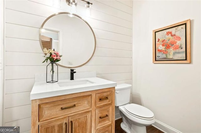 bathroom featuring vanity, wood walls, and toilet