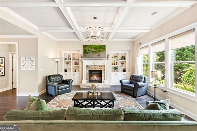 living area featuring wood finished floors, baseboards, a stone fireplace, coffered ceiling, and a notable chandelier