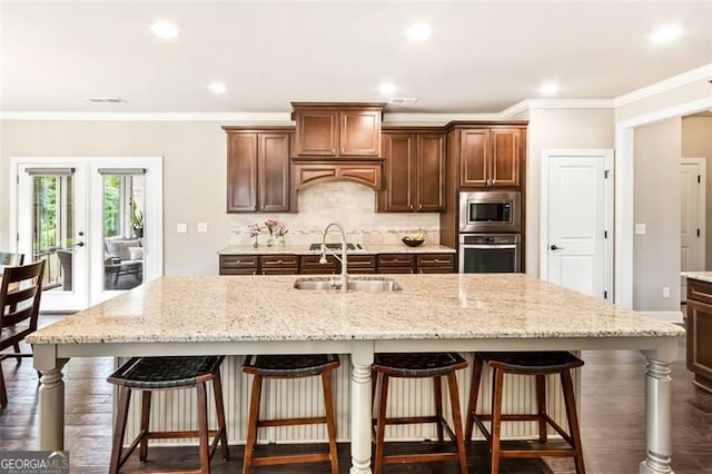 kitchen featuring light stone counters, a sink, an island with sink, stainless steel appliances, and backsplash