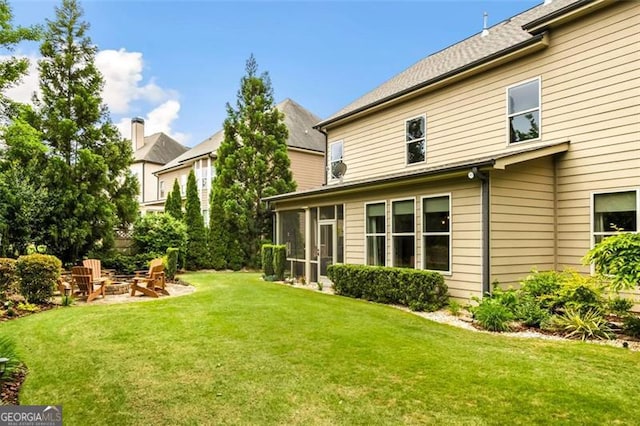 rear view of house featuring a lawn, a fire pit, and a sunroom