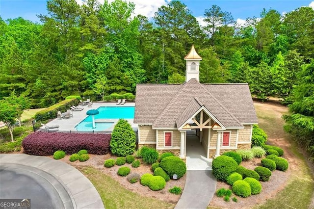 exterior space with a community pool, roof with shingles, and stone siding