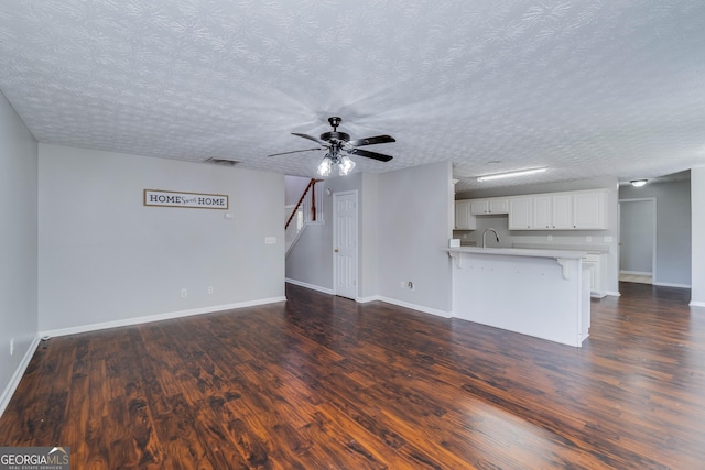 981 Charles Hall Dr, Dacula, GA 30019 - unfurnished living room featuring baseboards, ceiling fan, dark wood-type flooring, a textured ceiling, and a sink
