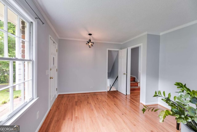 unfurnished room featuring baseboards, a textured ceiling, light wood finished floors, and ornamental molding