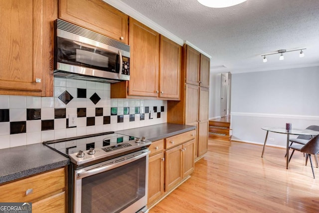 kitchen featuring dark countertops, appliances with stainless steel finishes, decorative backsplash, and light wood-style flooring