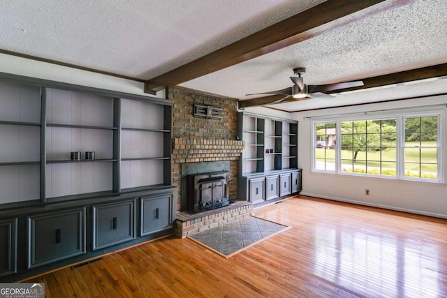 unfurnished living room with a ceiling fan, a textured ceiling, wood finished floors, and beamed ceiling