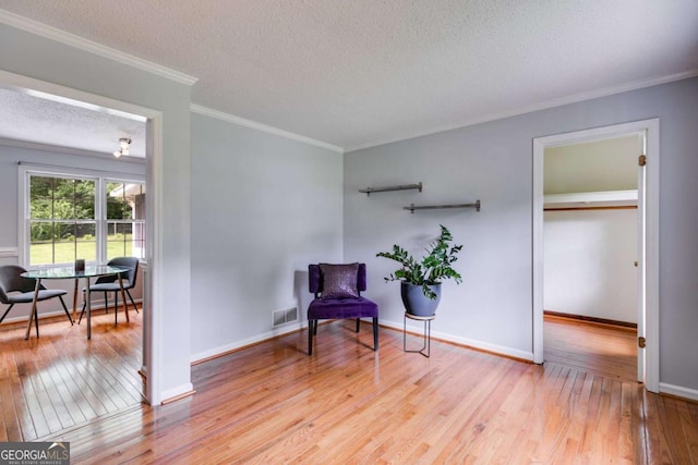 sitting room featuring visible vents, ornamental molding, baseboards, a textured ceiling, and light wood finished floors