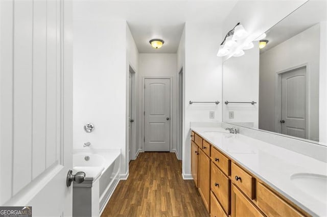 full bathroom featuring double vanity, a bath, wood finished floors, and a sink