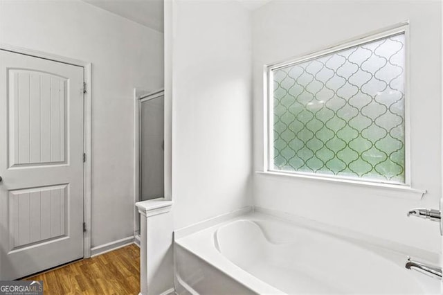 full bath with plenty of natural light, a shower stall, a bath, and wood finished floors