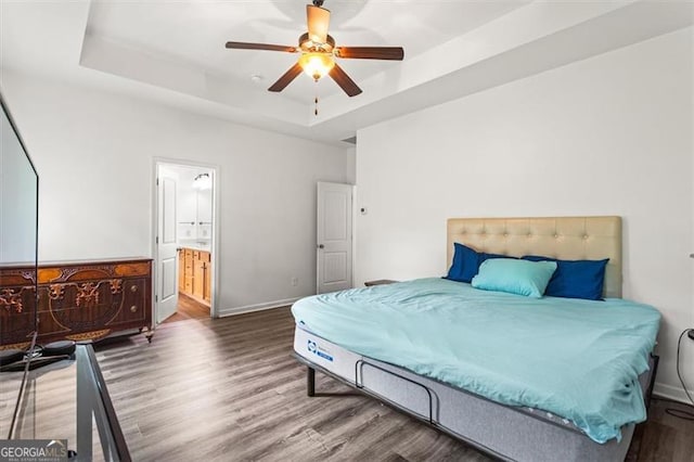 bedroom with wood finished floors, baseboards, ceiling fan, connected bathroom, and a tray ceiling