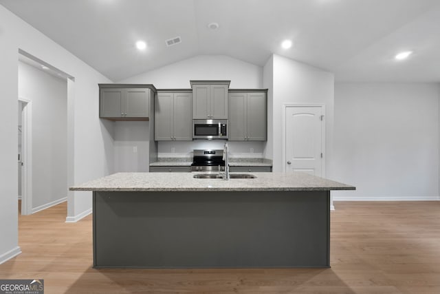 kitchen featuring appliances with stainless steel finishes, a center island with sink, a sink, baseboards, and lofted ceiling