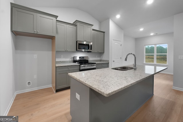kitchen with appliances with stainless steel finishes, a sink, light wood-style floors, a kitchen island with sink, and gray cabinetry