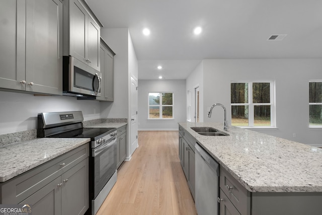 kitchen featuring a kitchen island with sink, stainless steel appliances, gray cabinets, and a sink