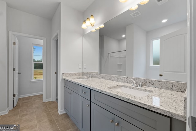 bathroom with visible vents, double vanity, a shower, baseboards, and a sink