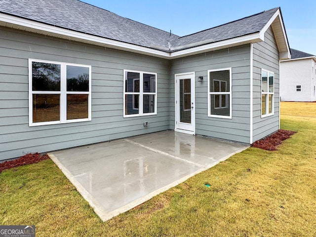 back of property with a lawn, a shingled roof, and a patio area
