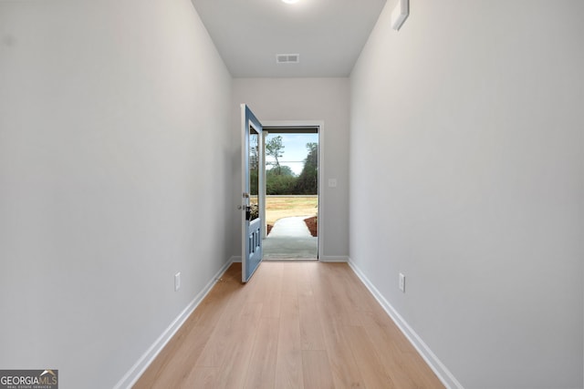 hallway with baseboards, light wood finished floors, and visible vents