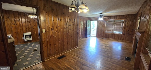 unfurnished dining area with wooden walls, heating unit, wood finished floors, and ceiling fan with notable chandelier