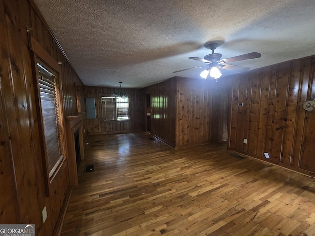 unfurnished room with wood-type flooring, wood walls, a textured ceiling, and ceiling fan
