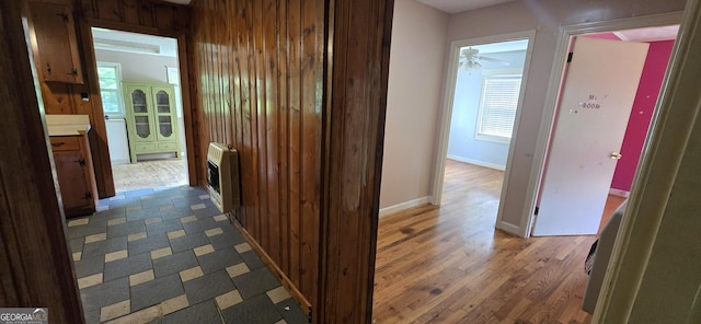 hallway featuring heating unit, baseboards, and wood finished floors