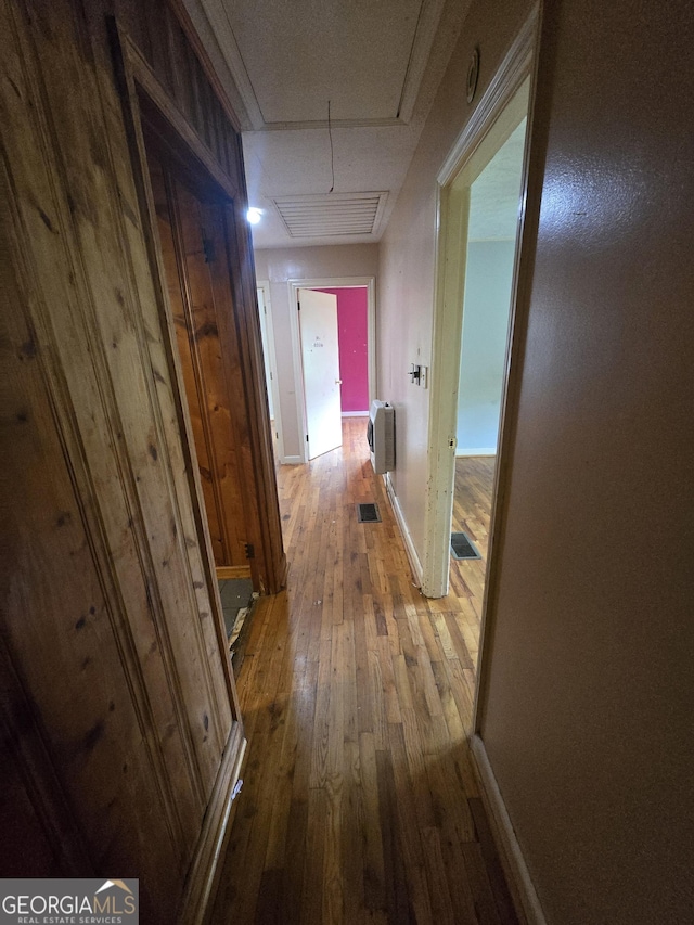 corridor featuring heating unit, baseboards, hardwood / wood-style floors, and visible vents