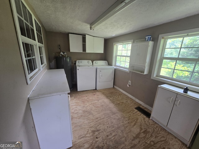 clothes washing area with a textured ceiling, visible vents, cabinet space, water heater, and washer and dryer