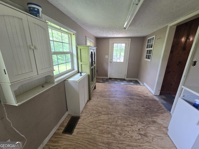 doorway with visible vents, a textured ceiling, and baseboards