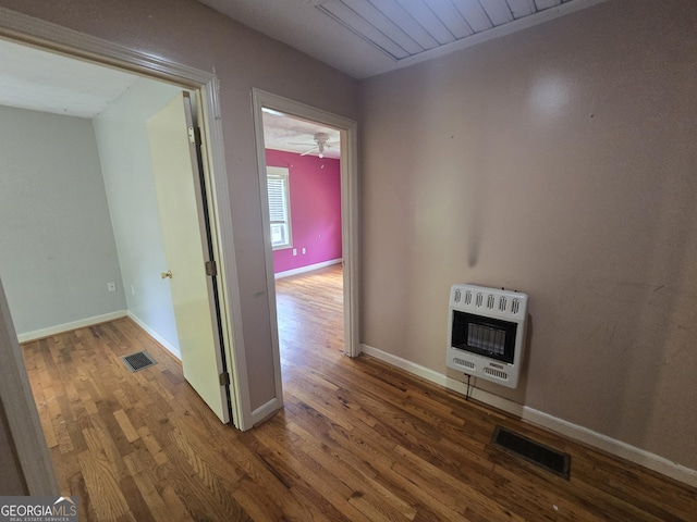 hallway featuring baseboards, heating unit, wood finished floors, and visible vents