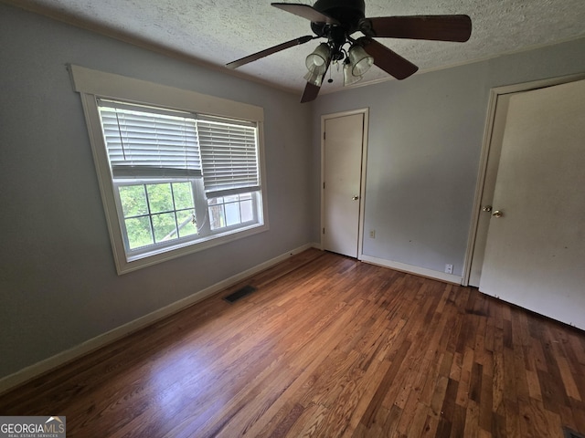 unfurnished bedroom with ceiling fan, a textured ceiling, baseboards, wood finished floors, and visible vents
