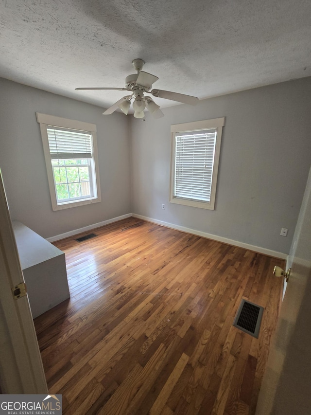 spare room with visible vents, a textured ceiling, baseboards, and wood finished floors