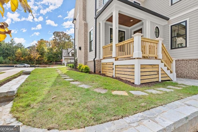 view of side of property featuring a lawn, covered porch, and brick siding