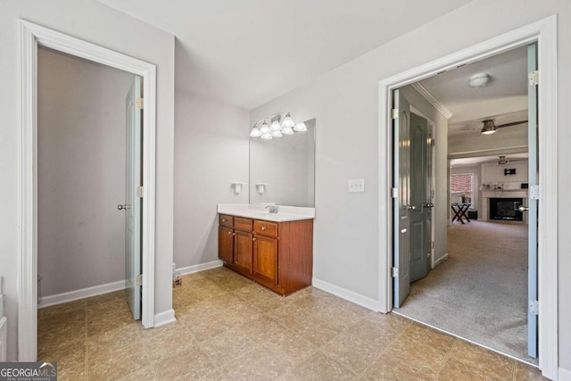 bathroom featuring ceiling fan, crown molding, vanity, baseboards, and a glass covered fireplace