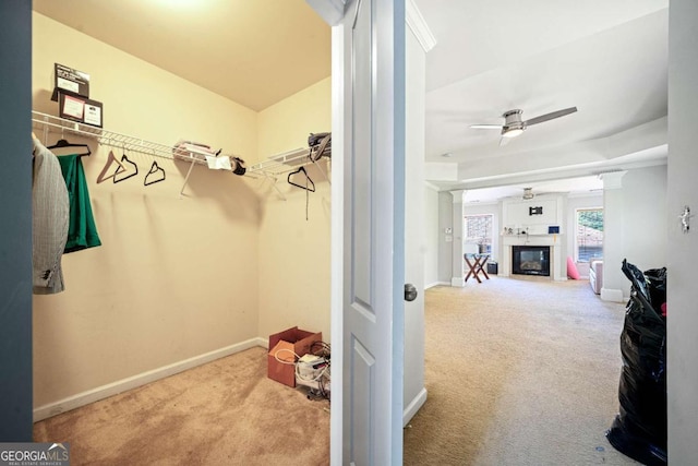 spacious closet with a glass covered fireplace, ceiling fan, carpet, and decorative columns