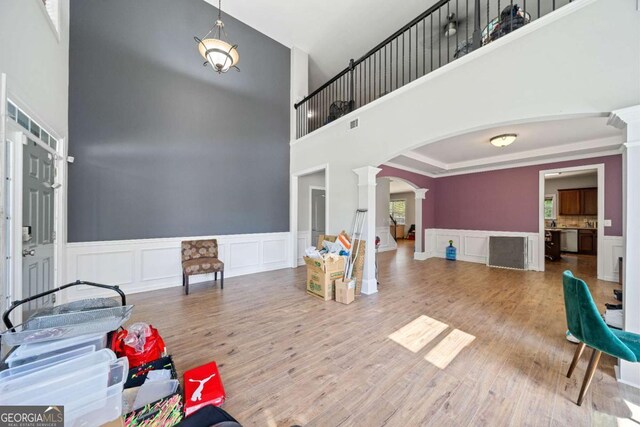 game room featuring a decorative wall, arched walkways, wood finished floors, a towering ceiling, and ornate columns