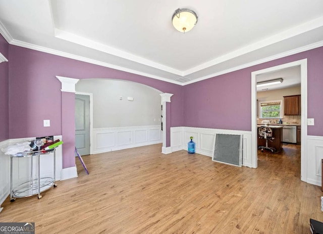 interior space with a tray ceiling, decorative columns, light wood finished floors, and a wainscoted wall