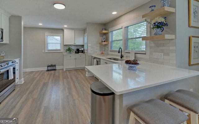 kitchen featuring open shelves, a sink, a kitchen breakfast bar, stainless steel appliances, and a peninsula