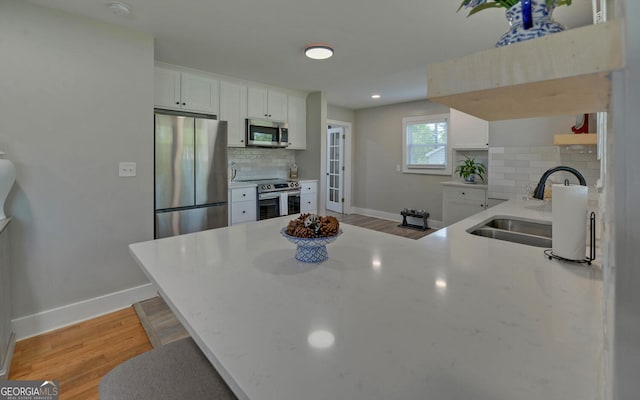kitchen featuring a sink, stainless steel appliances, baseboards, a peninsula, and decorative backsplash