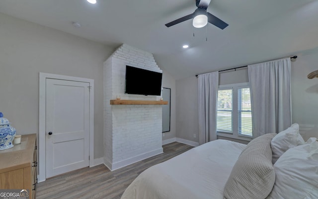 bedroom with ceiling fan, a large fireplace, wood finished floors, baseboards, and lofted ceiling
