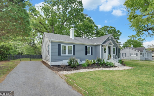 view of front of property with fence, a front yard, roof with shingles, a chimney, and driveway