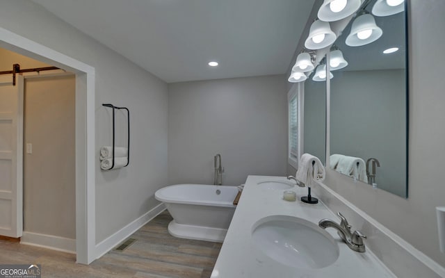 full bath featuring visible vents, double vanity, wood finished floors, a freestanding bath, and a sink