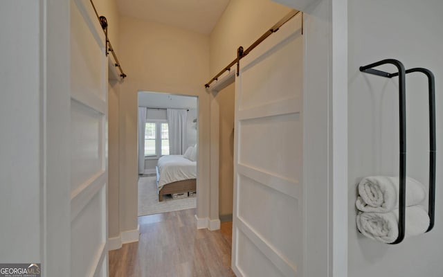 hall featuring baseboards, light wood-type flooring, and a barn door